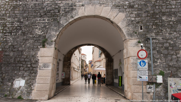 Large arched pedestrian passage through Zadar’s old stone fortifications leading into a narrow street.