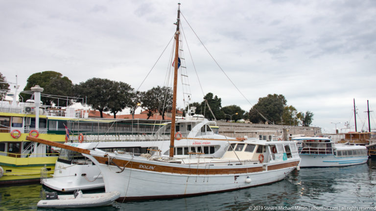 White single-masted excursion boat moored in Zadar harbor among other passenger vessels.