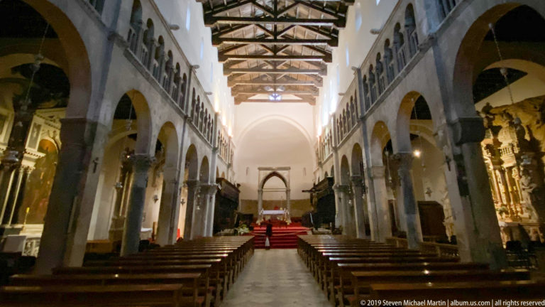 Central nave of St. Anastasia Cathedral with stone arcades, timber roof, side altars, pews, and raised sanctuary.