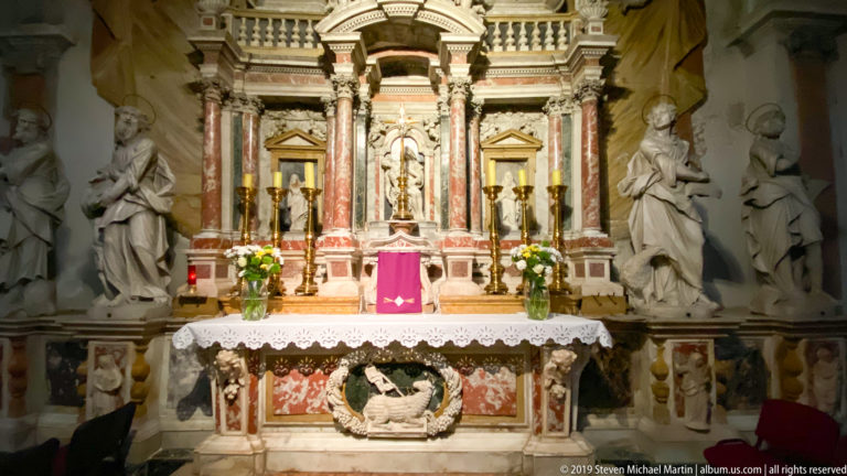 Rich marble side altar with red-veined columns, statues, candles, flowers, and a carved altar frontal.