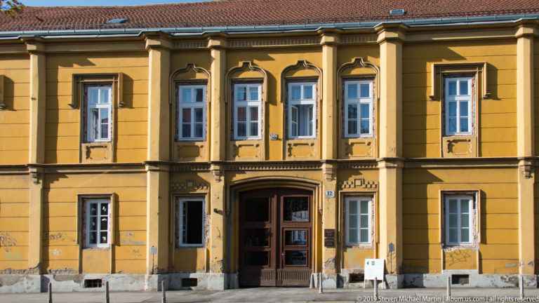 Ochre two-story historic building with symmetrical white-framed windows, central wooden doorway, decorative trim, and graffiti at street level.