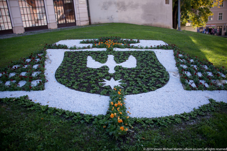 Formal flowerbed designed as a green-and-white heraldic emblem with a central symbol and star, edged by flowers.
