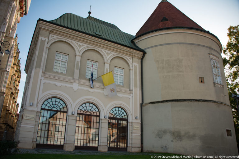 Pale Baroque building beside a large round defensive tower with a steep roof in Zagreb’s cathedral precinct.