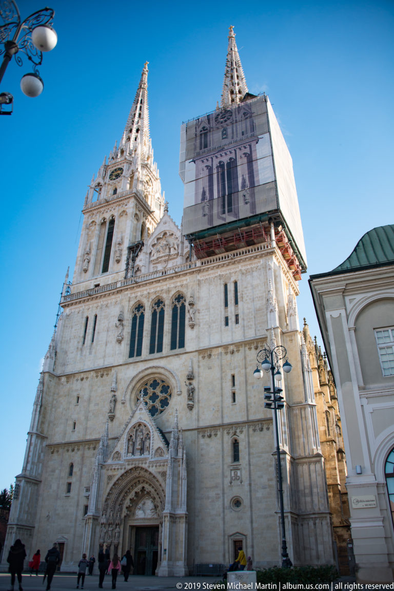 Low-angle view of Zagreb Cathedral’s ornate west façade, with twin towers and one tower covered by restoration screening.