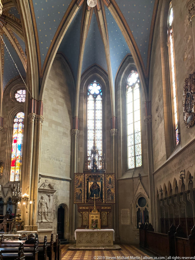 Wide Gothic side chapel with painted altar, tall windows, choir stalls, wall monuments, and blue ribbed ceiling.