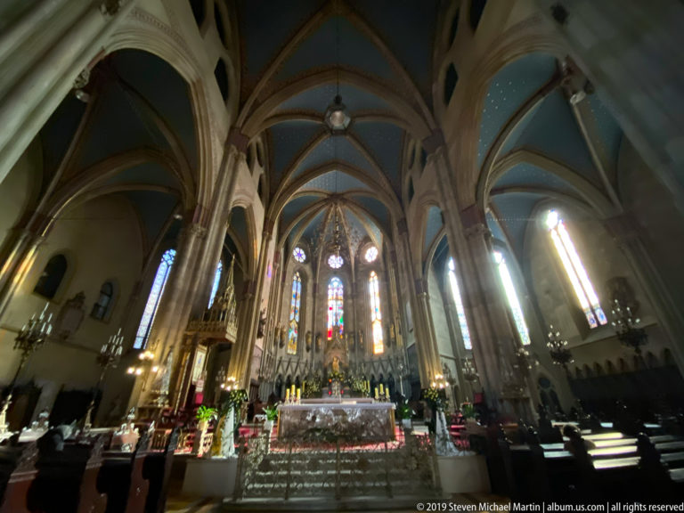 Wide-angle view up the nave of Zagreb Cathedral toward the altar, showing ribbed vaults, stained glass, and pews.