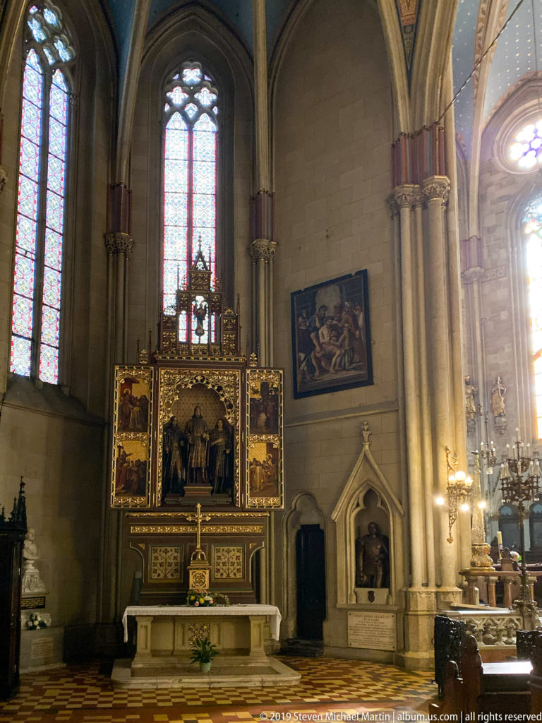 Gothic side chapel with tall windows, painted retable, stone altar, clustered columns, and wall monuments.