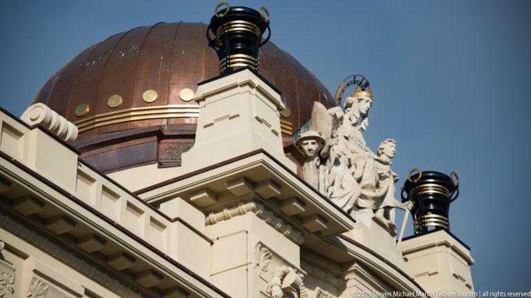 Low-angle view of the Mimara Museum roof with copper dome, central female sculpture, smaller figures, and black finials.