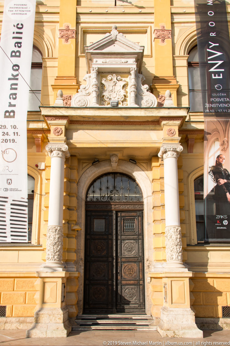 Ornate arched entrance of the Mimara Museum with paired columns, carved stonework, and dark wooden doors.