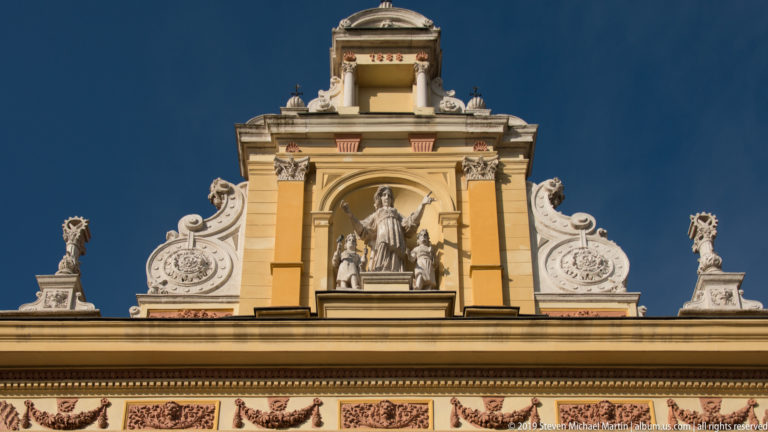 Upper façade of the Mimara Museum with columns, scrollwork, statues, and a central standing female figure against blue sky.