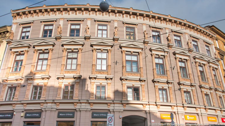 Ornate curved corner building with tall windows, pilasters, cornices, and ground-floor shops in central Zagreb.