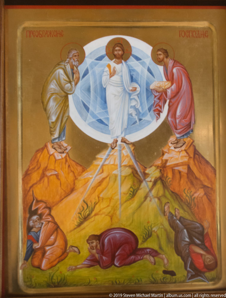 Orthodox icon of the Transfiguration with Christ in white between two prophets above disciples on a rocky mountain.