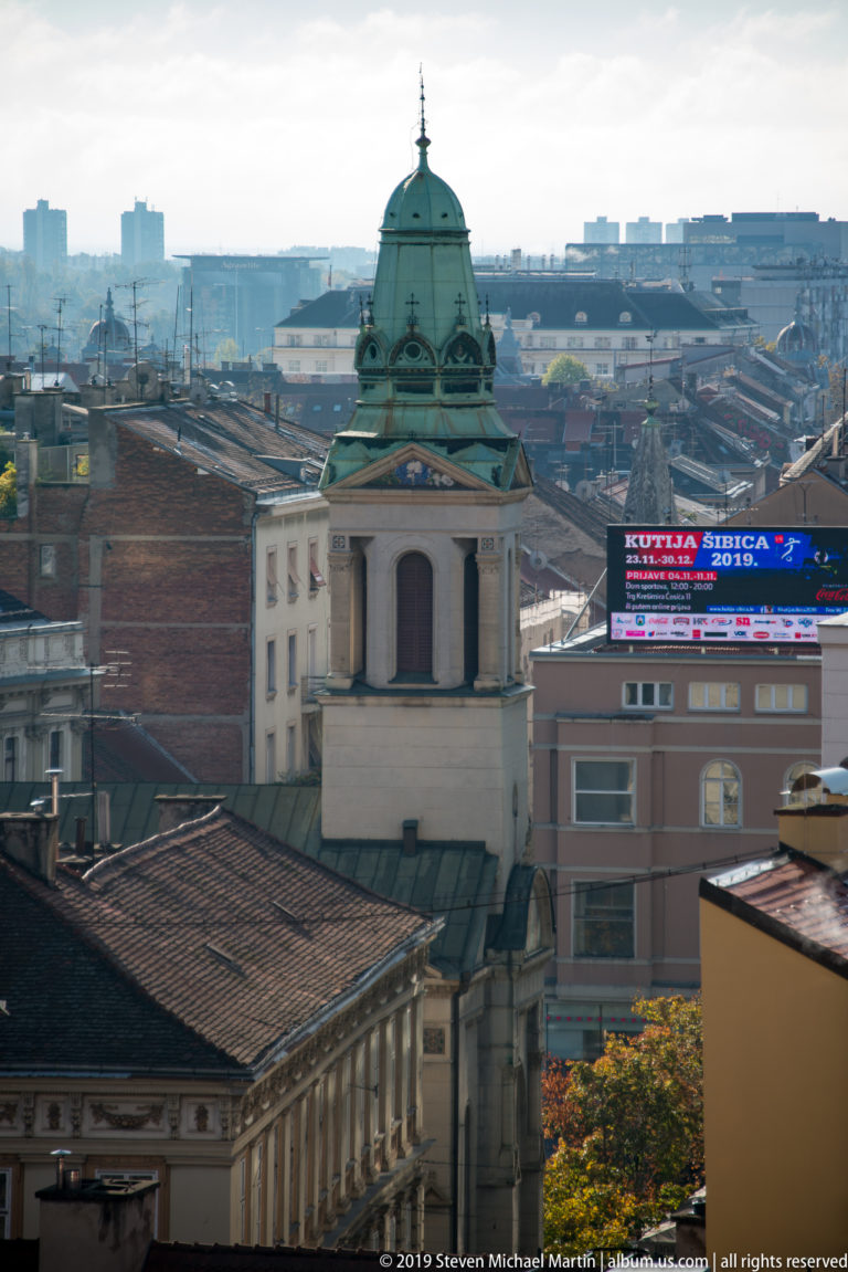 Green copper-domed rooftop pavilion with classical detailing rises above red-tiled roofs in central Zagreb.