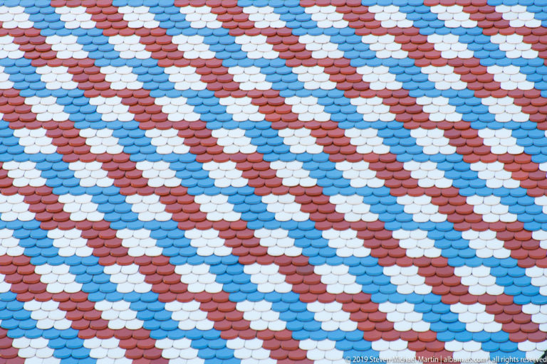 Tight detail of scalloped red, white, light-blue, and dark-blue glazed tiles arranged in diagonal bands on St. Mark’s Church.