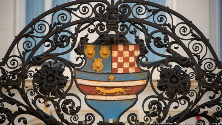 Decorative black wrought-iron grille surrounding a painted heraldic shield with Croatian red-and-white checks and blue-gold motifs.