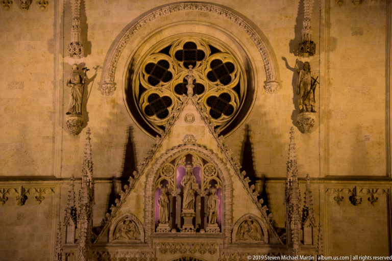 Rose window above the ornate main portal of Zagreb Cathedral, with flanking statues, pinnacles, reliefs, and violet-lit niches.