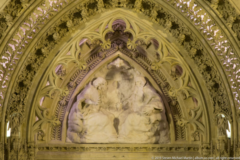 Pointed tympanum relief at Zagreb Cathedral surrounded by layered Gothic foliage, tracery, and small carved figures.