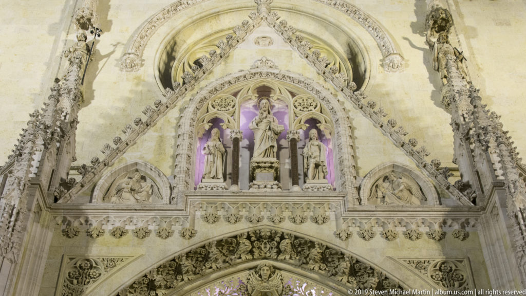 Upper portal of Zagreb Cathedral with saints in niches, pointed arches, relief panels, pinnacles, and pale stone lit at night.
