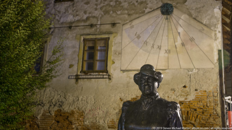 Bronze statue of Marija Jurić Zagorka beneath a large wall sundial with Roman numerals on Tkalčićeva Street at night.