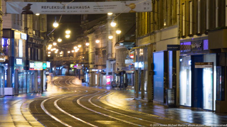Curving tram tracks run along an empty illuminated Zagreb shopping street lined with historic buildings and storefronts at night.