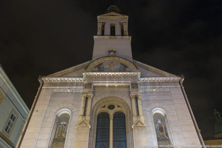 Front façade of Zagreb’s Orthodox cathedral at night, with arched portal, saint images, pediment, and bell tower.