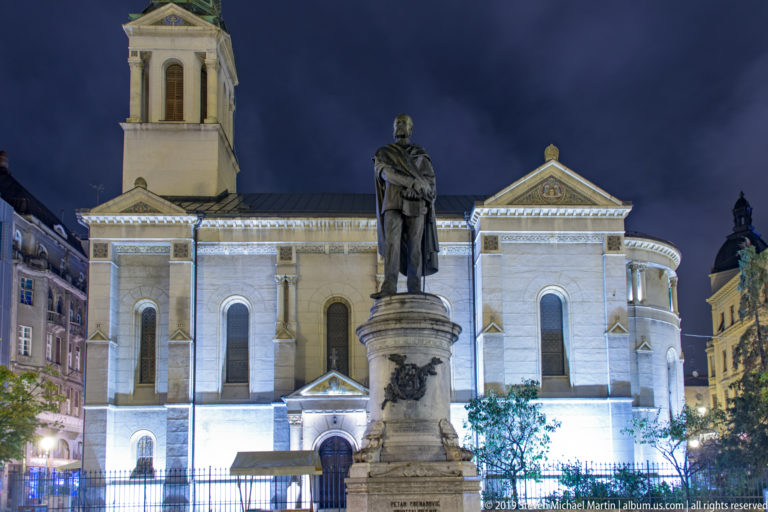 Petar Preradović statue on a tall pedestal centered before the illuminated Orthodox cathedral in Zagreb at night.