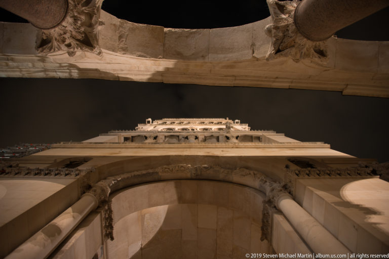 Upward night view through pale stone arches and columns toward the illuminated upper architecture of Saint Domnius Cathedral in Split.