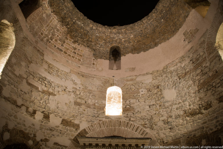 Circular stone interior of Diocletian’s Palace Vestibule with an open oculus, arched windows, and illuminated masonry at night.