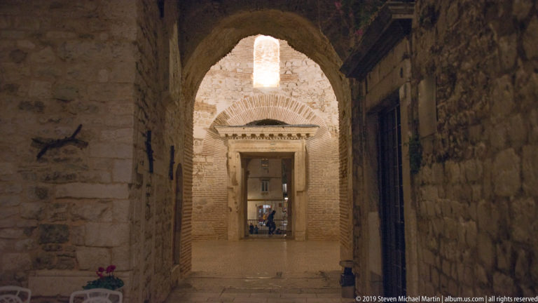 Vaulted brick-and-stone passage in Diocletian’s Palace with a large rectangular stone doorway aligned beneath an arch.