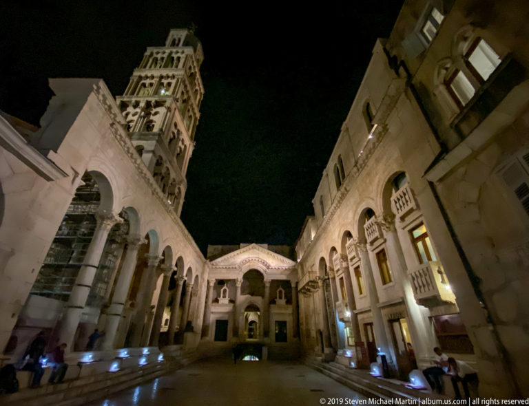 Wide-angle night view across the Peristyle with Saint Domnius bell tower above the left colonnade and façades on the right.