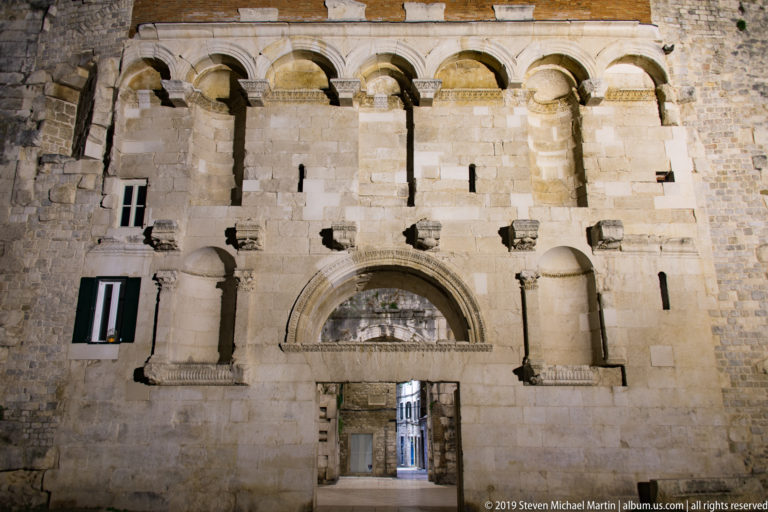 Floodlit Golden Gate of Diocletian’s Palace with central doorway, large blind arch, niches, and shallow upper arcades.