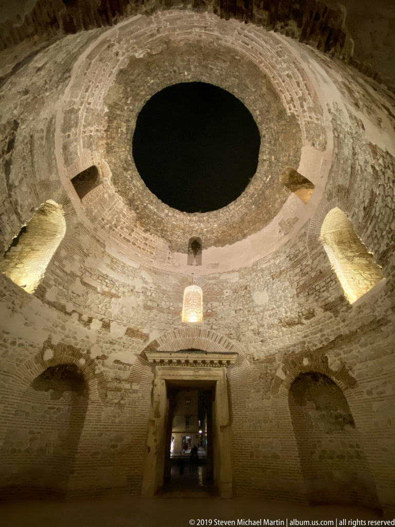 Wide interior view of Diocletian’s Palace Vestibule showing circular masonry walls, recessed arches, and a large open oculus.