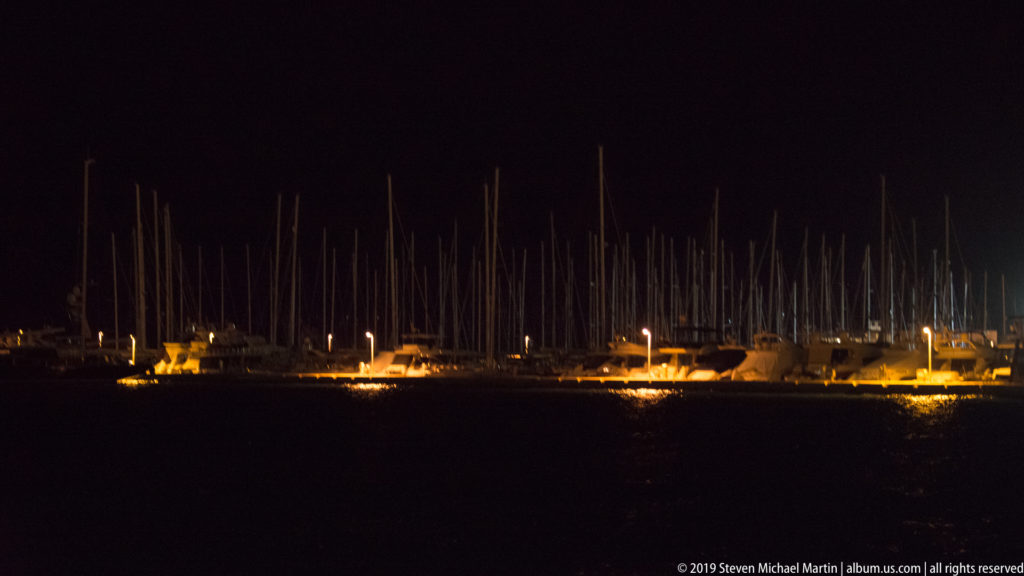 Rows of sailboat masts and moored vessels silhouetted against the night, with amber lights along Split’s waterfront.