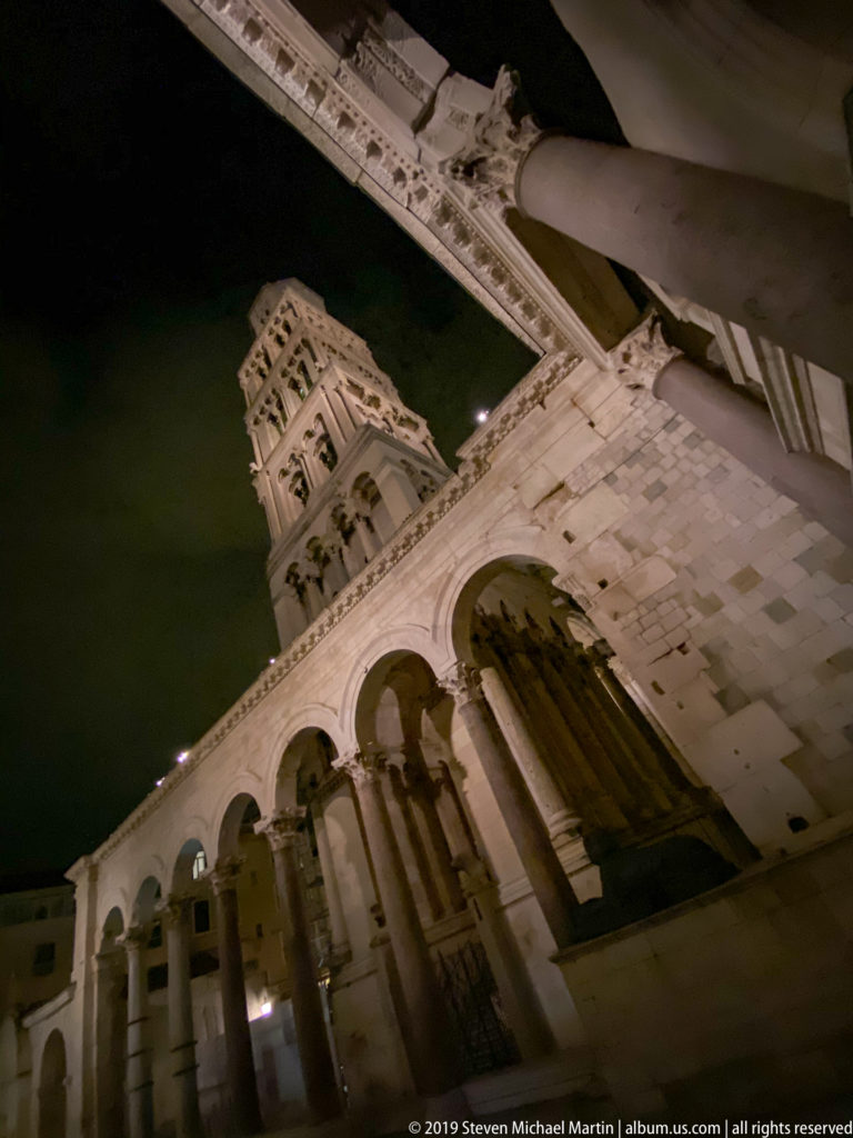 Tilted night view of Peristyle arches and columns with Saint Domnius bell tower rising in the background.