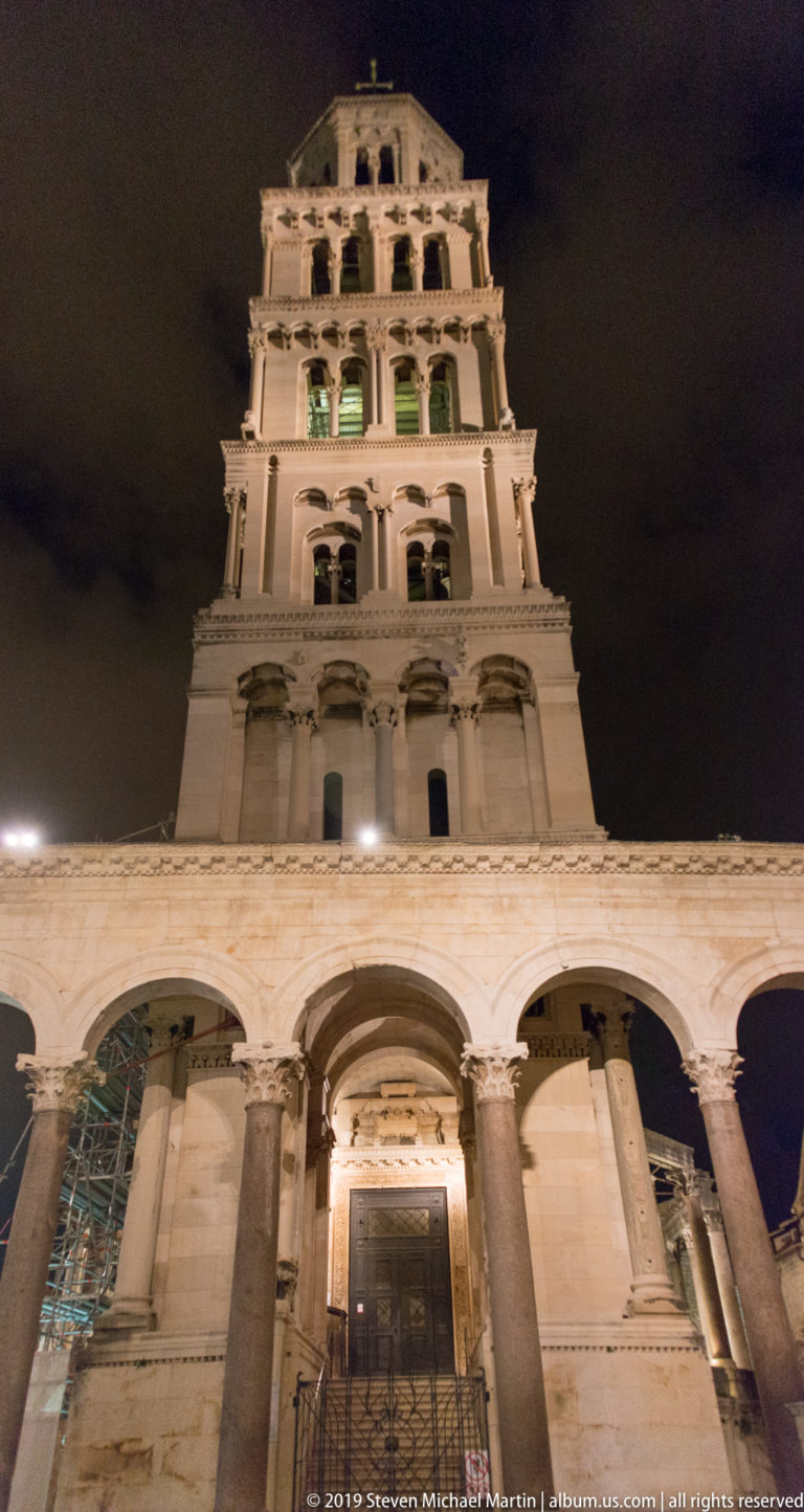 Front night view of Saint Domnius bell tower with stacked arcades rising above the Peristyle and cathedral entrance.