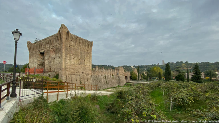 Massive brick tower and long crenellated wall of the Ponte Visconteo extending across the landscape at Borghetto.