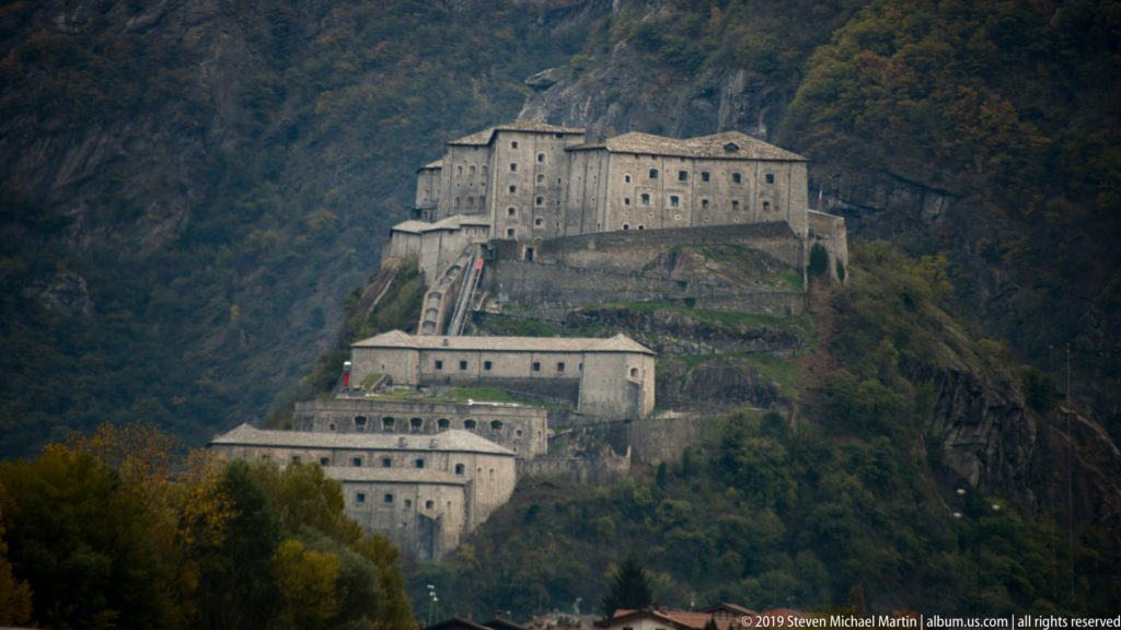 Forte di Bard fortress terraces climbing a steep wooded mountainside above the Aosta Valley.