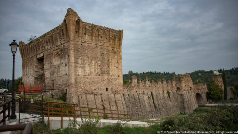 Close view of a massive brick Ponte Visconteo tower with crenellated bridge wall extending toward an arched passage.