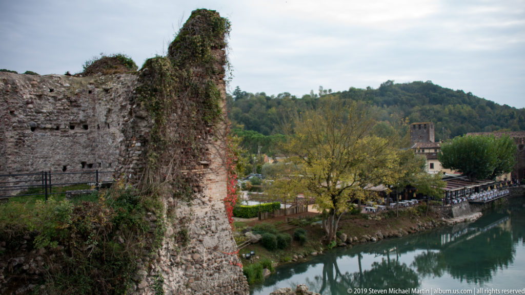 Weathered stone-and-brick fortification ruin overlooking the Mincio River and trees near Borghetto.