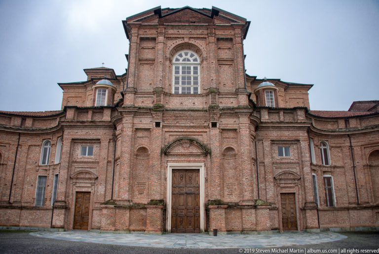 Frontal brick façade of the Church of Sant'Uberto with tall arched window, central doorway, pilasters, and curved side bays.