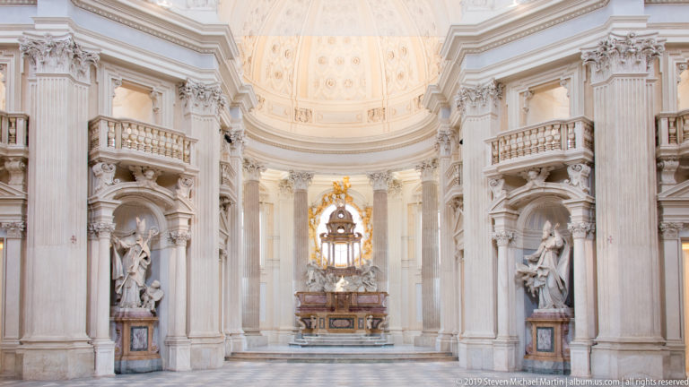 Axial view inside the Church of Sant'Uberto toward the ornate altar beneath the pale dome.