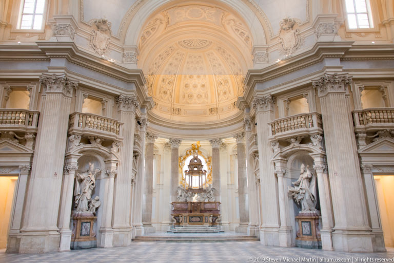 Symmetrical interior of the Church of Sant'Uberto with giant pilasters, side statues, domed ceiling, and central altar.