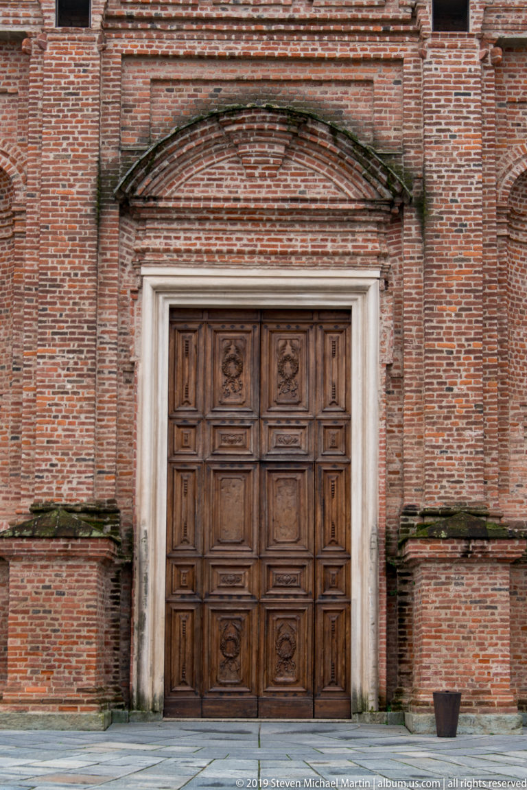 Paneled wooden doorway beneath a shallow curved brick pediment in the weathered red-brick palace façade.