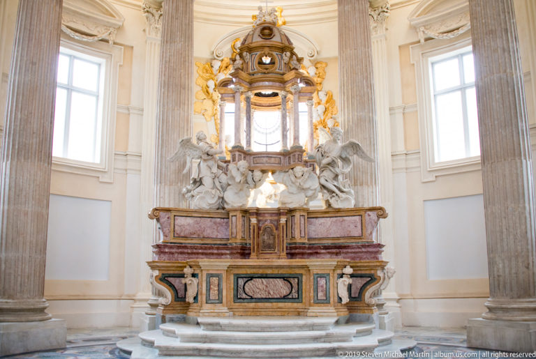 Polychrome altar with gilded upper structure, white sculptures, and giant columns inside the Church of Sant'Uberto.