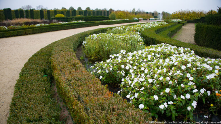 Curving bed of white flowers bordered by low clipped box hedges and pale gravel paths in the formal garden.
