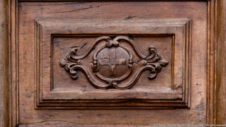 Close view of a carved wooden door panel with central heraldic shield and scrolling ornament.