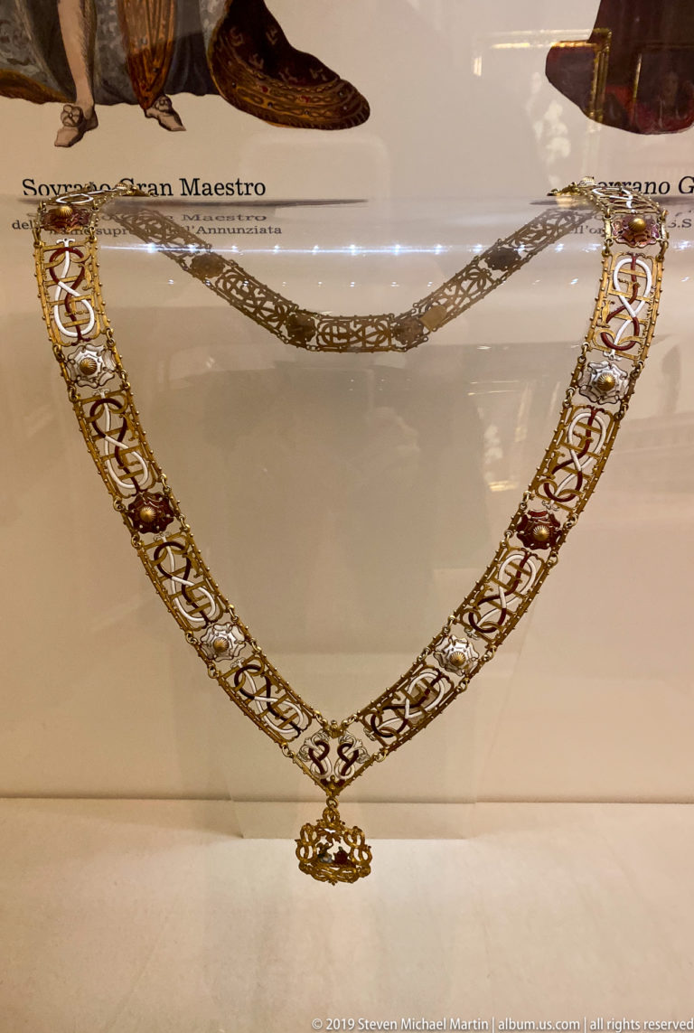 Full ceremonial collar arranged in a U shape, with repeating gold, white, and red links and a pendant at center.