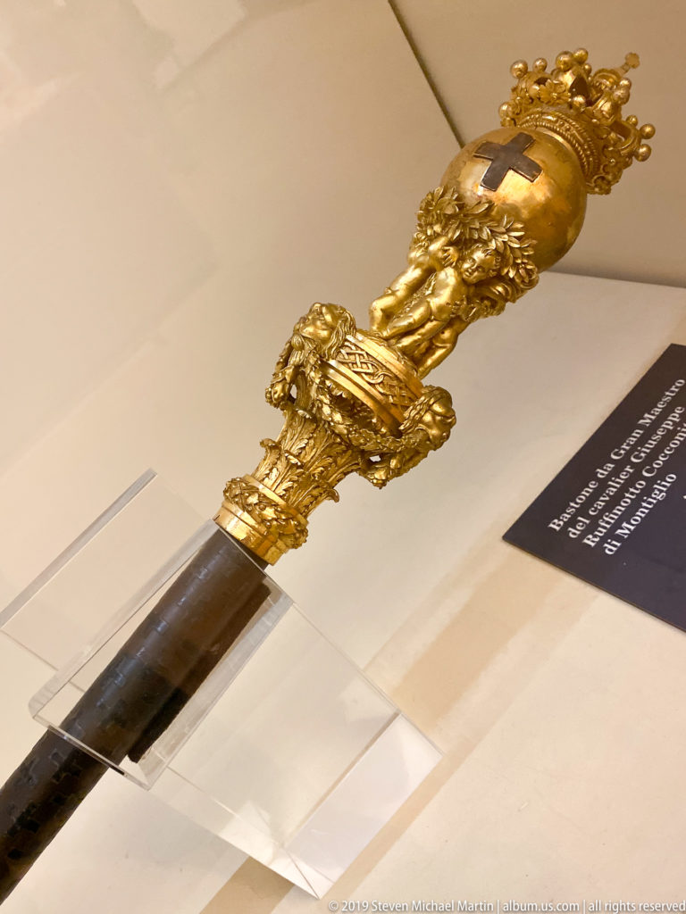 Close view of an ornate ceremonial sword hilt with gilded relief decoration and a crowned bearded head forming the pommel.