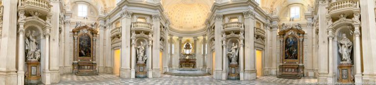 Bright Baroque chapel interior with tall pale piers, arches, side altars, sculptures, and a luminous vaulted central space.