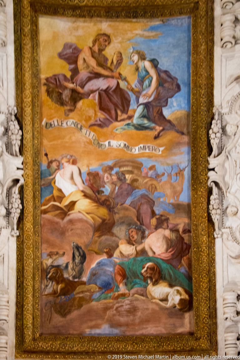 Large framed ceiling painting with many figures on clouds and below, surrounded by gilding and white stucco.